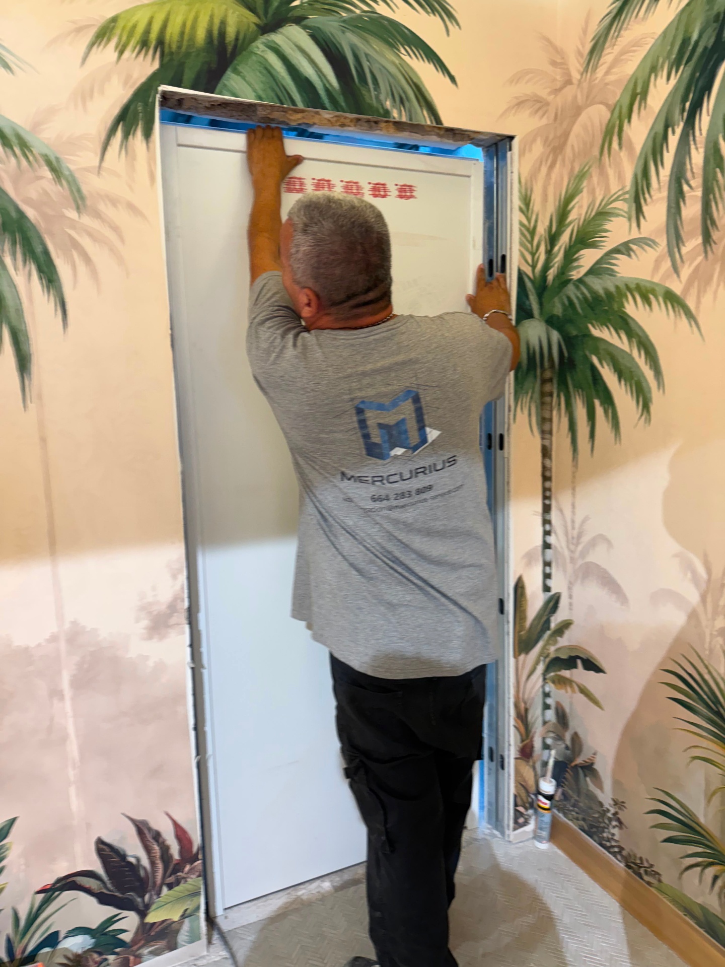 Operario Mercurius instalando puerta de pladur sobre pared con mural tropical